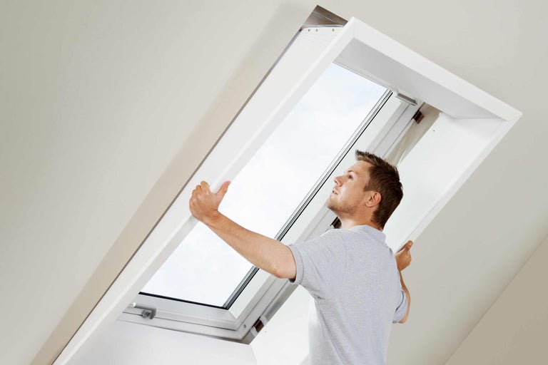 Un bărbat instalează o fereastră de mansardă în pod.