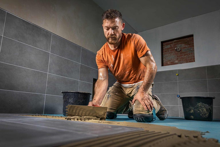 Faiantar la lucru: Așezarea plăcilor ceramice cu o spatulă și o găleată într-o baie.