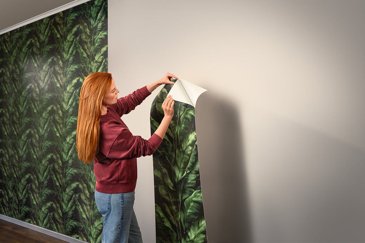 Femeie aplică un tapet vlies cu model vegetal pe perete
