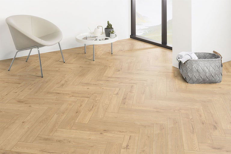 Cameră luminoasă cu parchet în spic, fotoliu, masă și coș