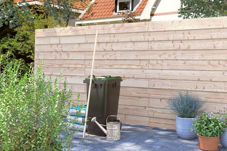 Gard din lemn în grădină cu coș de gunoi, stropitoare și plante