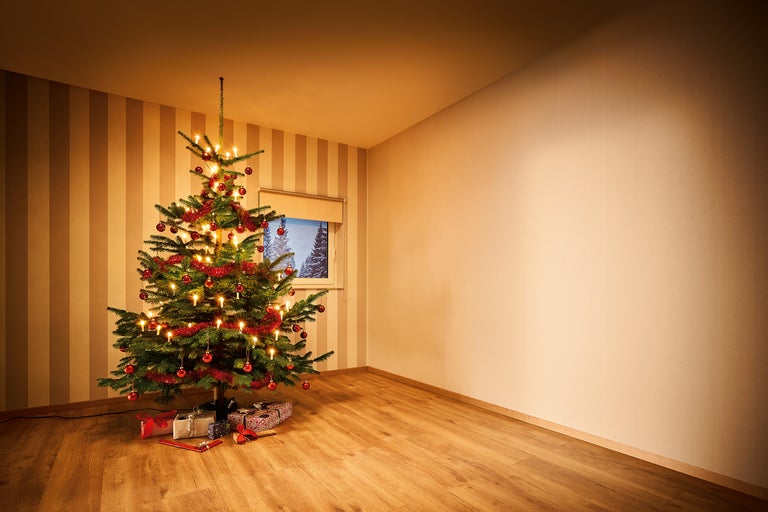 Cameră de Crăciun cu brad împodobit și cadouri pe podea de lemn.