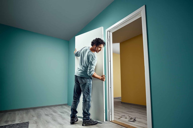 Un bărbat montează o ușă interioară albă într-o cameră renovată