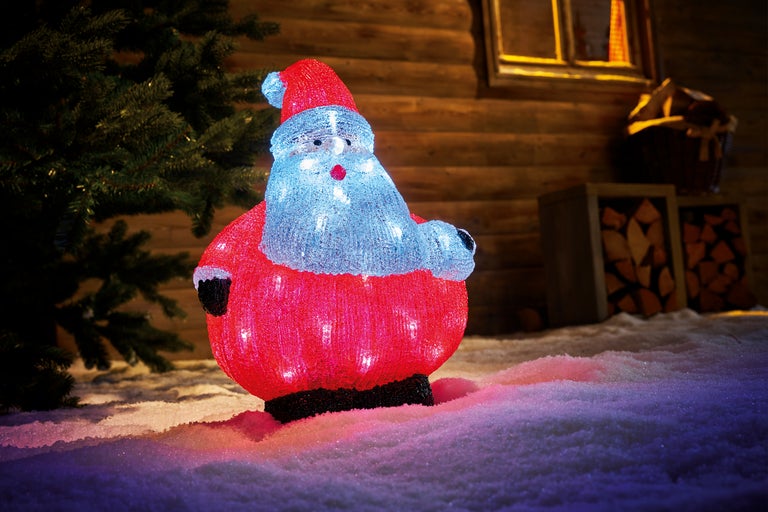 Figurină luminoasă a lui Moș Crăciun în zăpadă în fața unei case din lemn