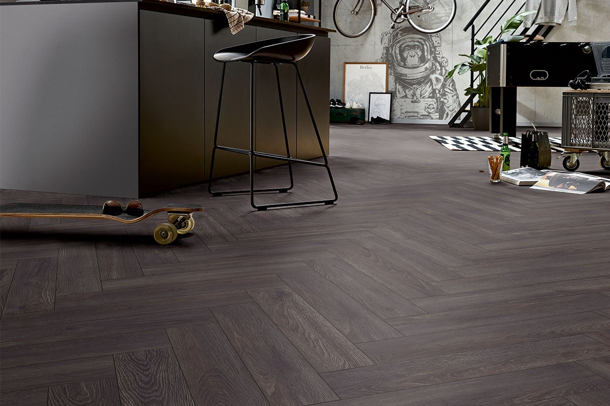 Interior cu podea din lemn închis la culoare, cu model herringbone, completat de o insulă de bucătărie, un scaun de bar și elemente decorative