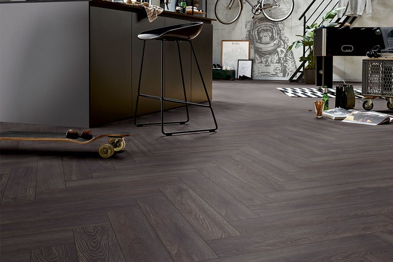 Interior cu podea din lemn închis la culoare, cu model herringbone, completat de o insulă de bucătărie, un scaun de bar și elemente decorative