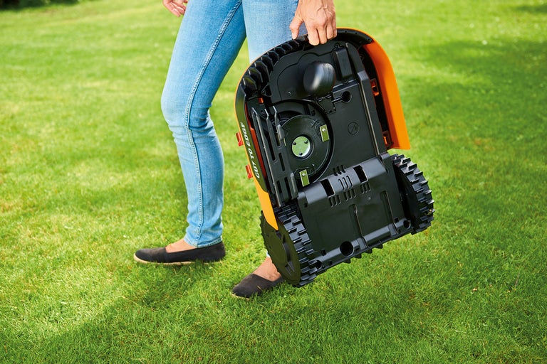 O persoană poartă un robot de tuns iarba pe un gazon.