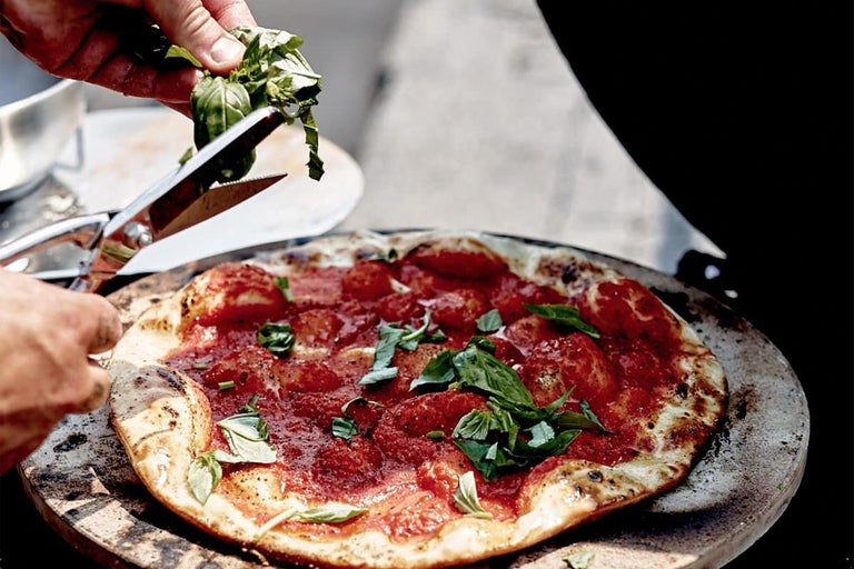 Pizza cu roșii și busuioc este garnită cu o foarfecă.