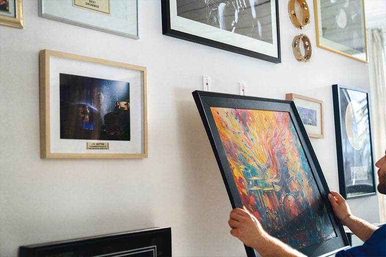 Persoană care atârnă opere de artă înrămate pe perete cu bandă adezivă pentru a crea o galerie.