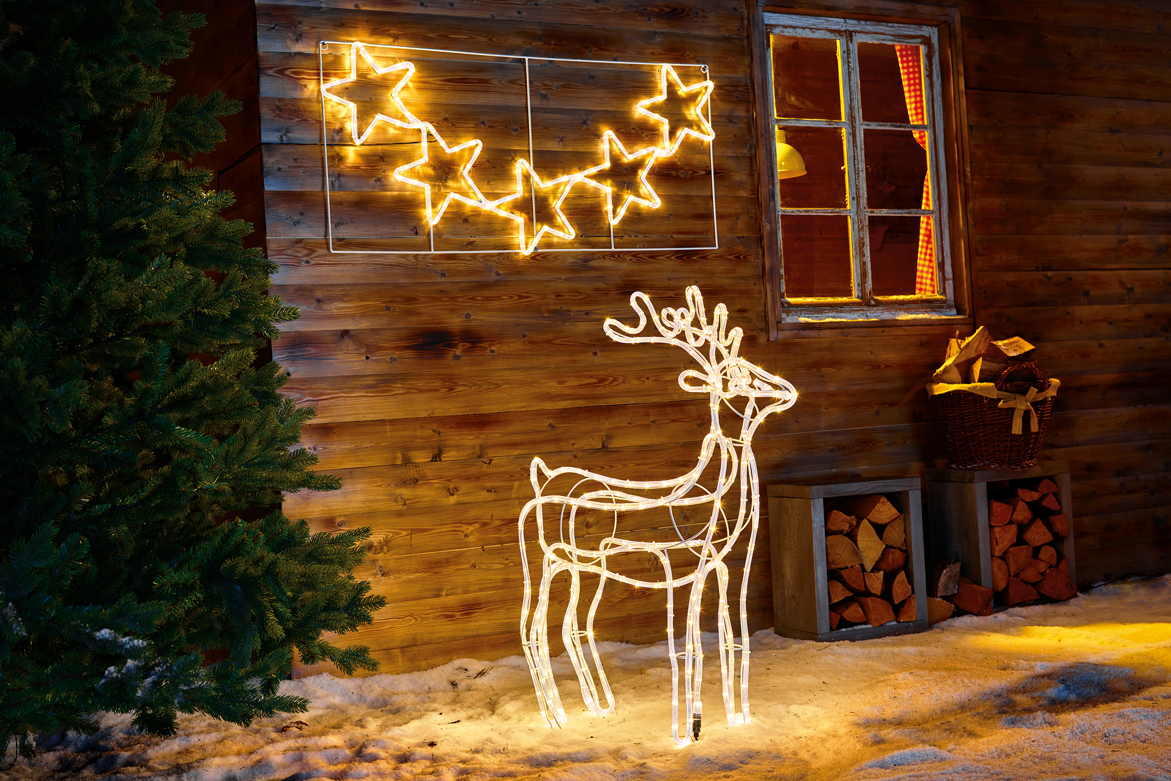 Aranjament decorativ cu motiv luminos stea și ren în fața unui perete de lemn