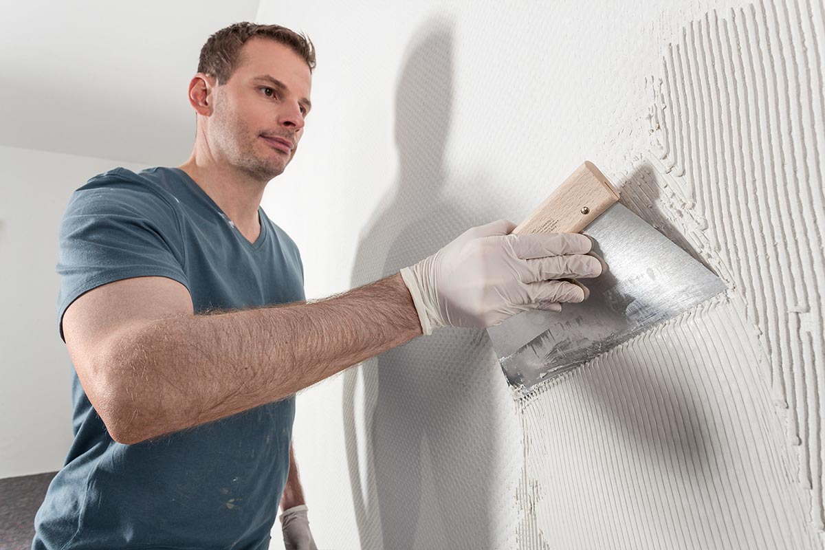 Un bărbat aplică adeziv pe un perete cu o mistrie