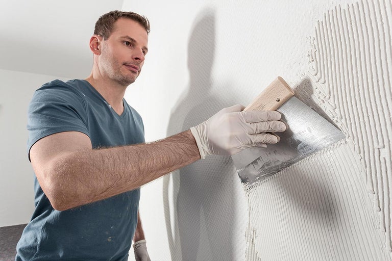 Un bărbat aplică adeziv pe un perete cu o mistrie