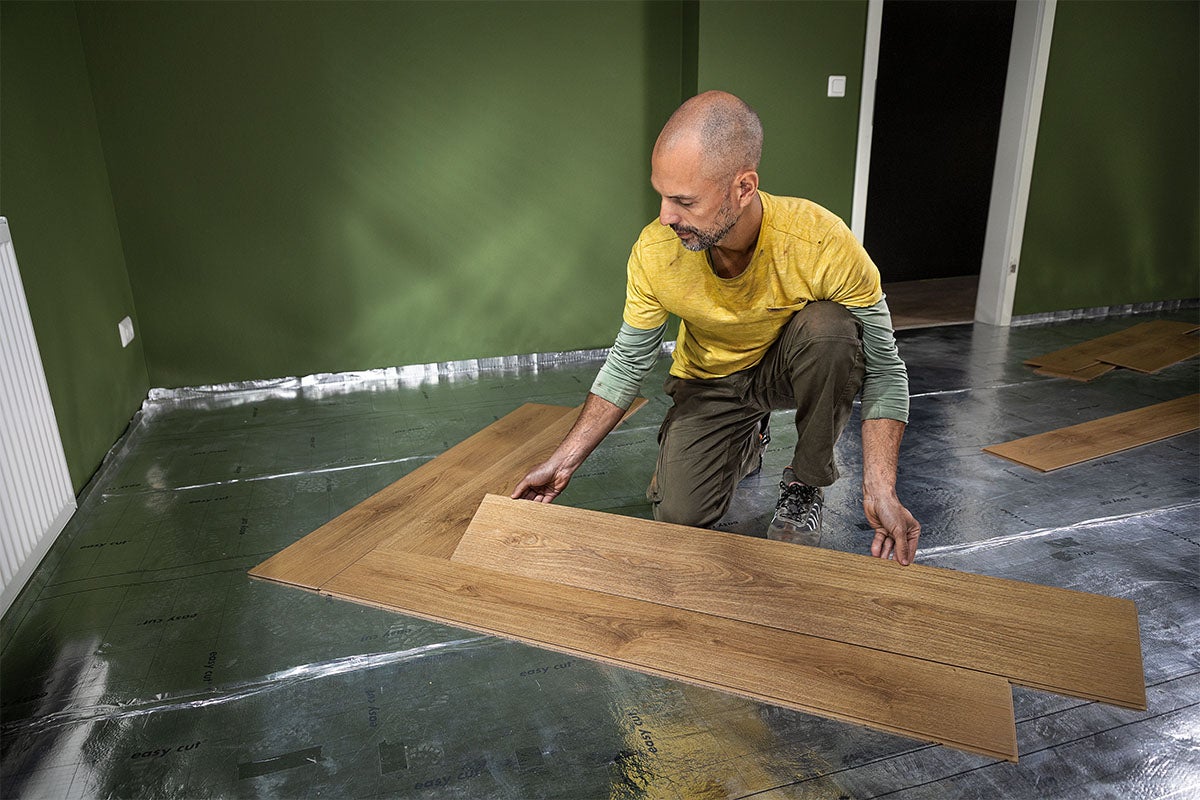 Un bărbat montează parchet laminat pe un strat izolator într-o cameră.
