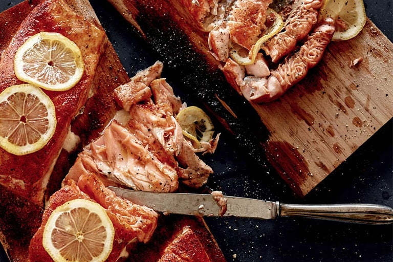 Somon la grătar pe scândură de lemn cu felii de lămâie și un cuțit.