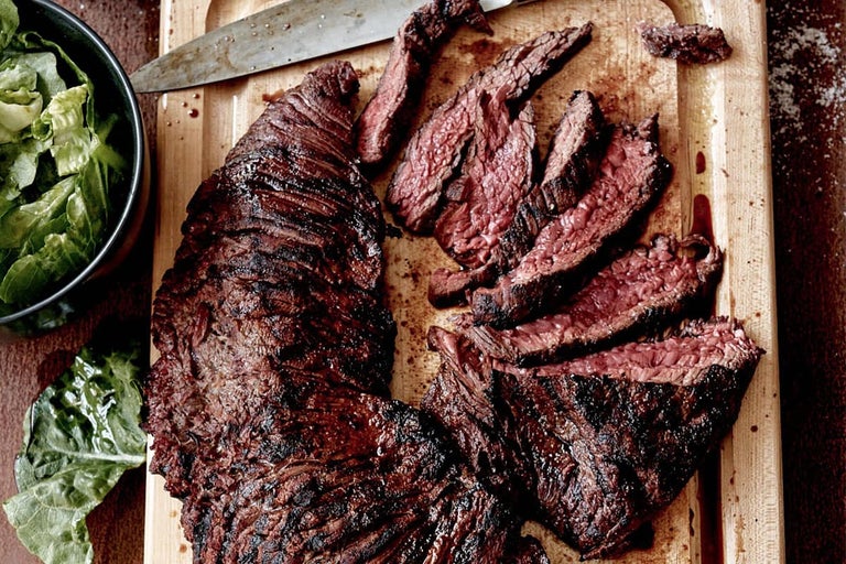 Carne de vită la grătar și feliată pe un tocător de lemn cu salată