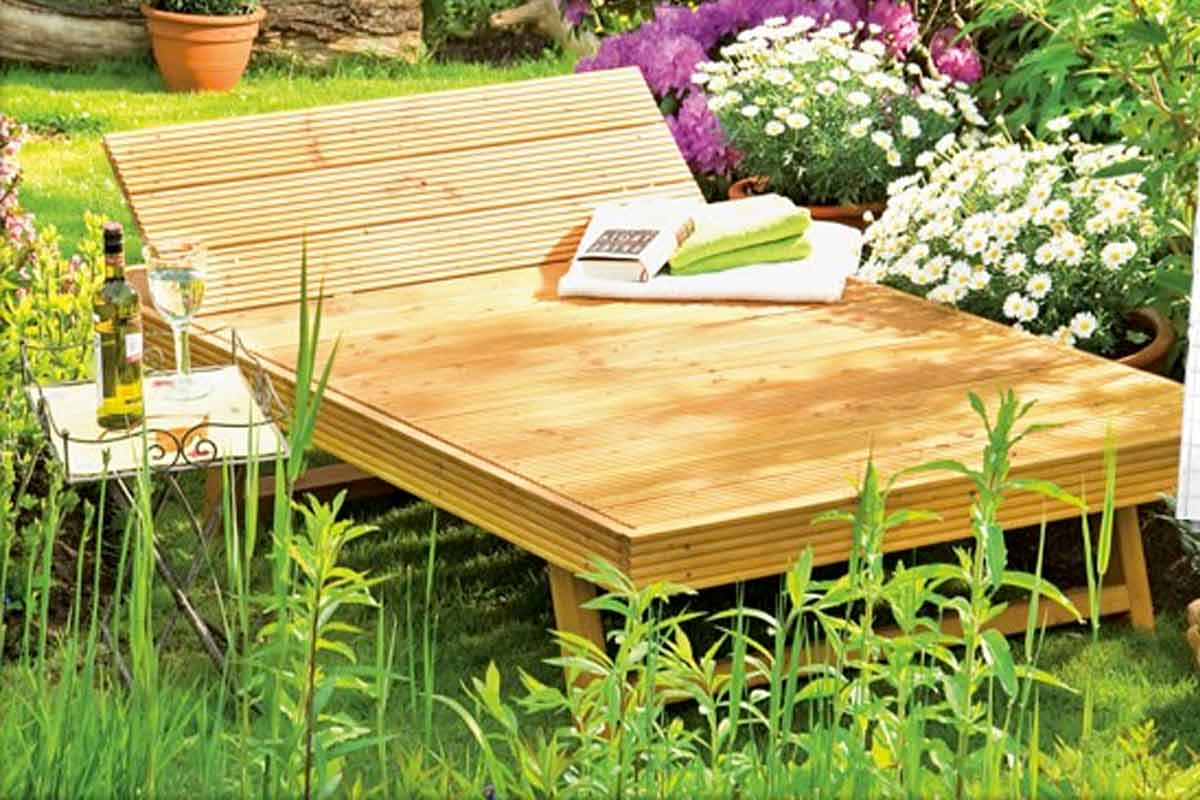 Șezlong din lemn în grădină cu măsuță laterală, băutură și plante
