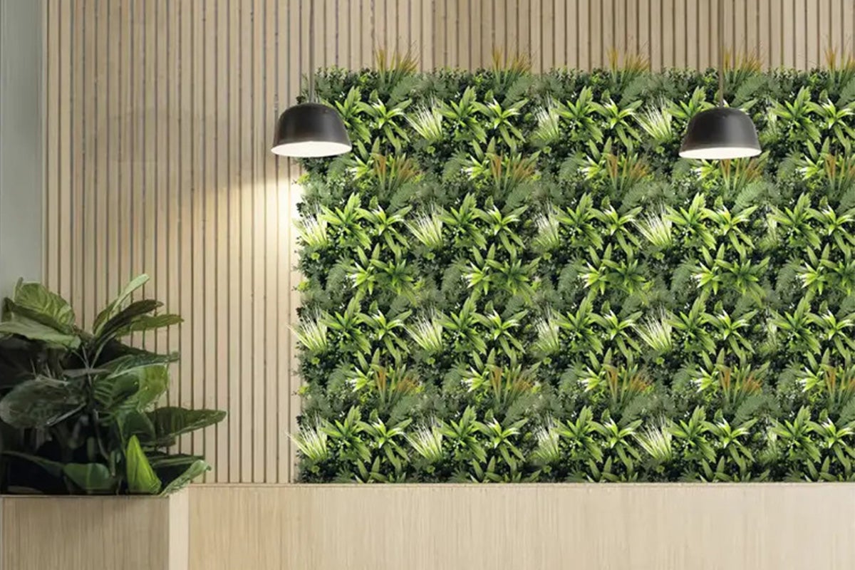 Perete decorativ cu plante artificiale, două lămpi suspendate și un ghiveci cu o plantă de interior