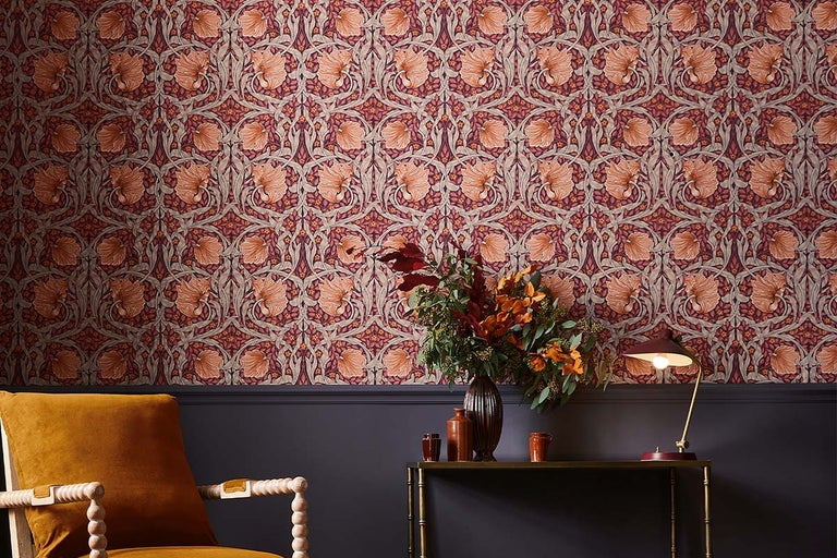 Cameră decorativă cu tapet cu model floral, fotoliu, masă cu vază de flori și lampă de masă.