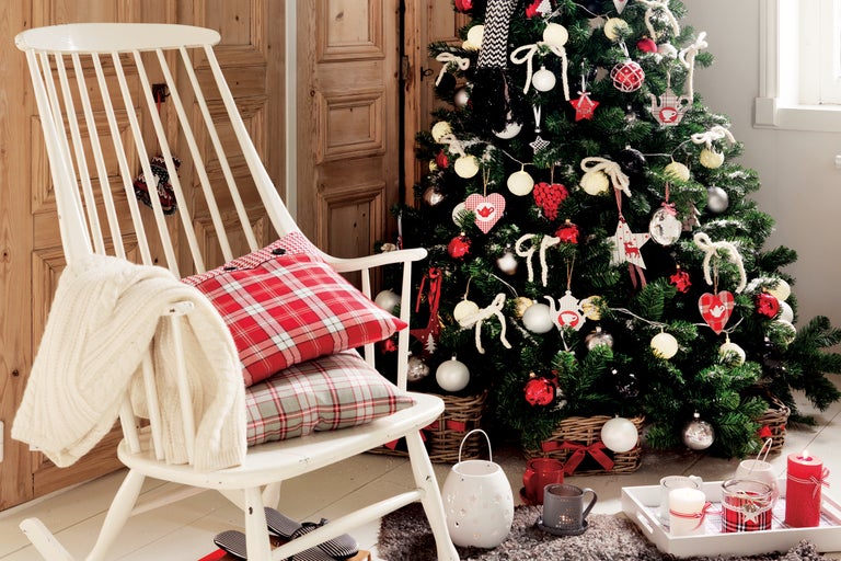 Scenă de Crăciun cu un brad împodobit, un balansoar cu perne și o tavă decorativă cu lumânări