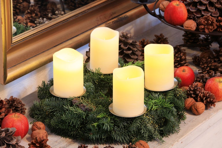 Coroană de advent cu patru lumânări, conuri de pin, mere și nuci ca decor festiv.