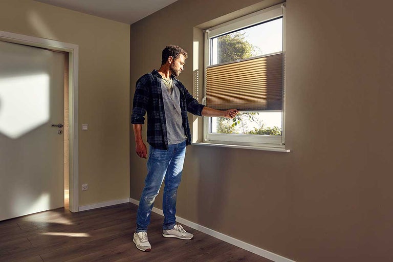 Bărbat care operează un jaluzele plisate pe fereastră într-o cameră.