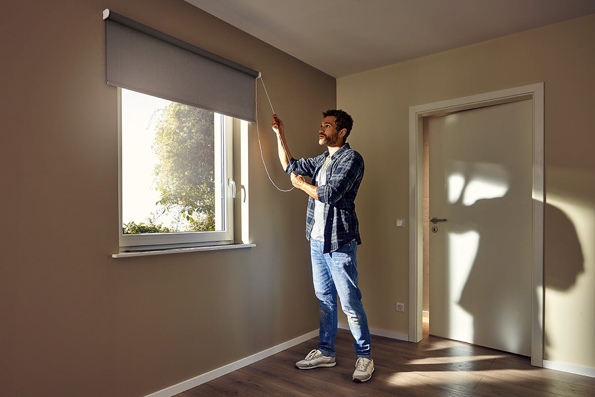 Un bărbat manevrează o rulou la fereastră într-o cameră.