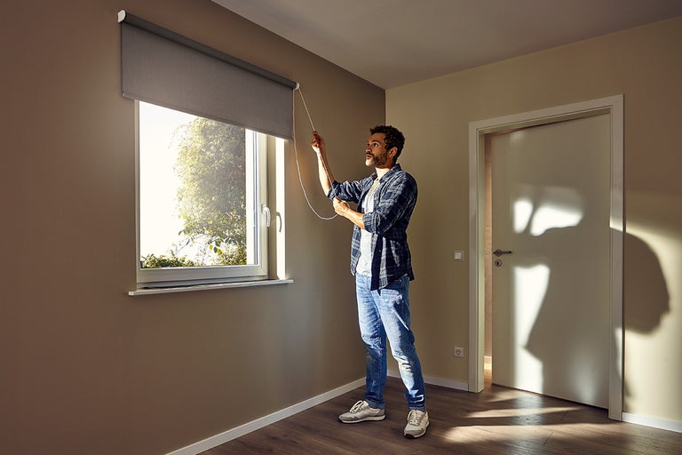 Un bărbat manevrează o rulou la fereastră într-o cameră.