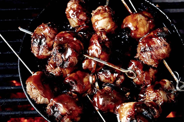 Bucăți de carne înfipte pe frigărui cu sos pe un grătar.