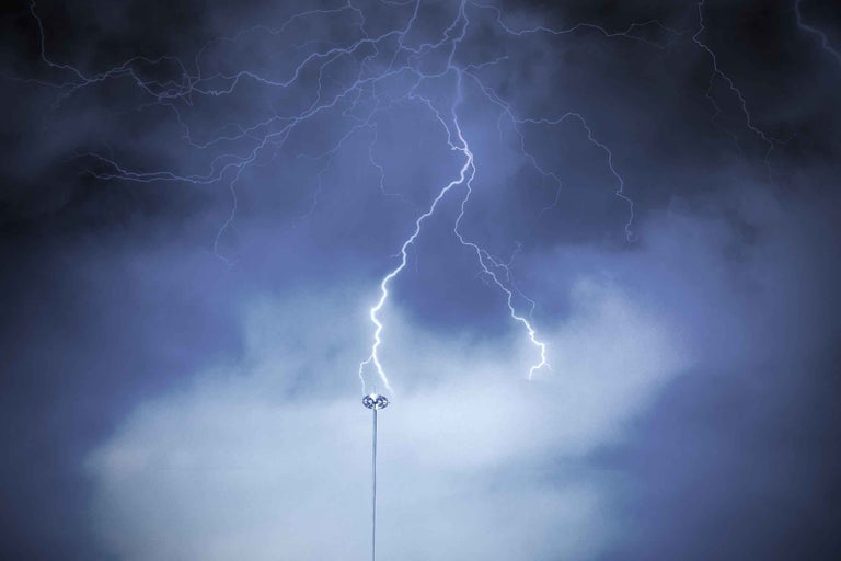 Trăsnet care lovește un paratrăsnet pe un stâlp înalt în timpul unei furtuni cu fulgere ramificate.