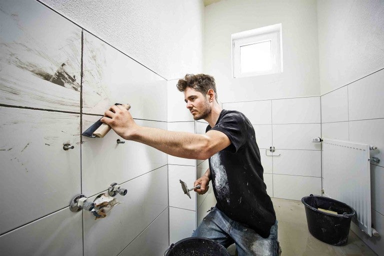 Bărbat chitind faianța în baie.