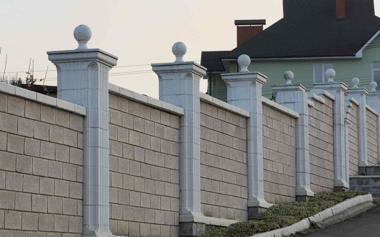 Un zid de grădină din blocuri de beton cu stâlpi și ornamente sferice.