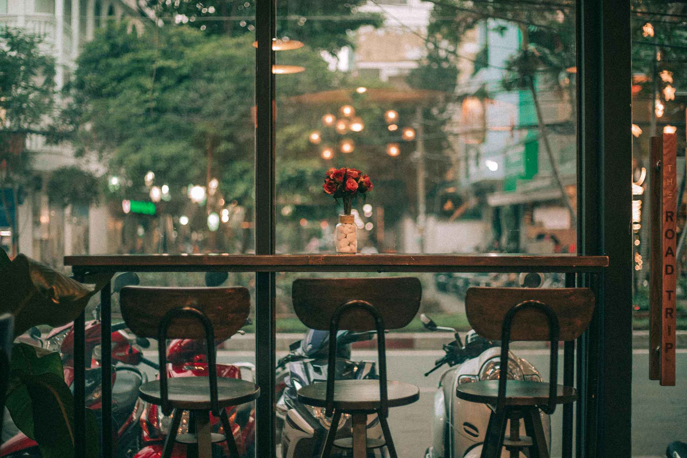 Vedere printr-o fereastră spre un bar cu scaune și o vază cu trandafiri