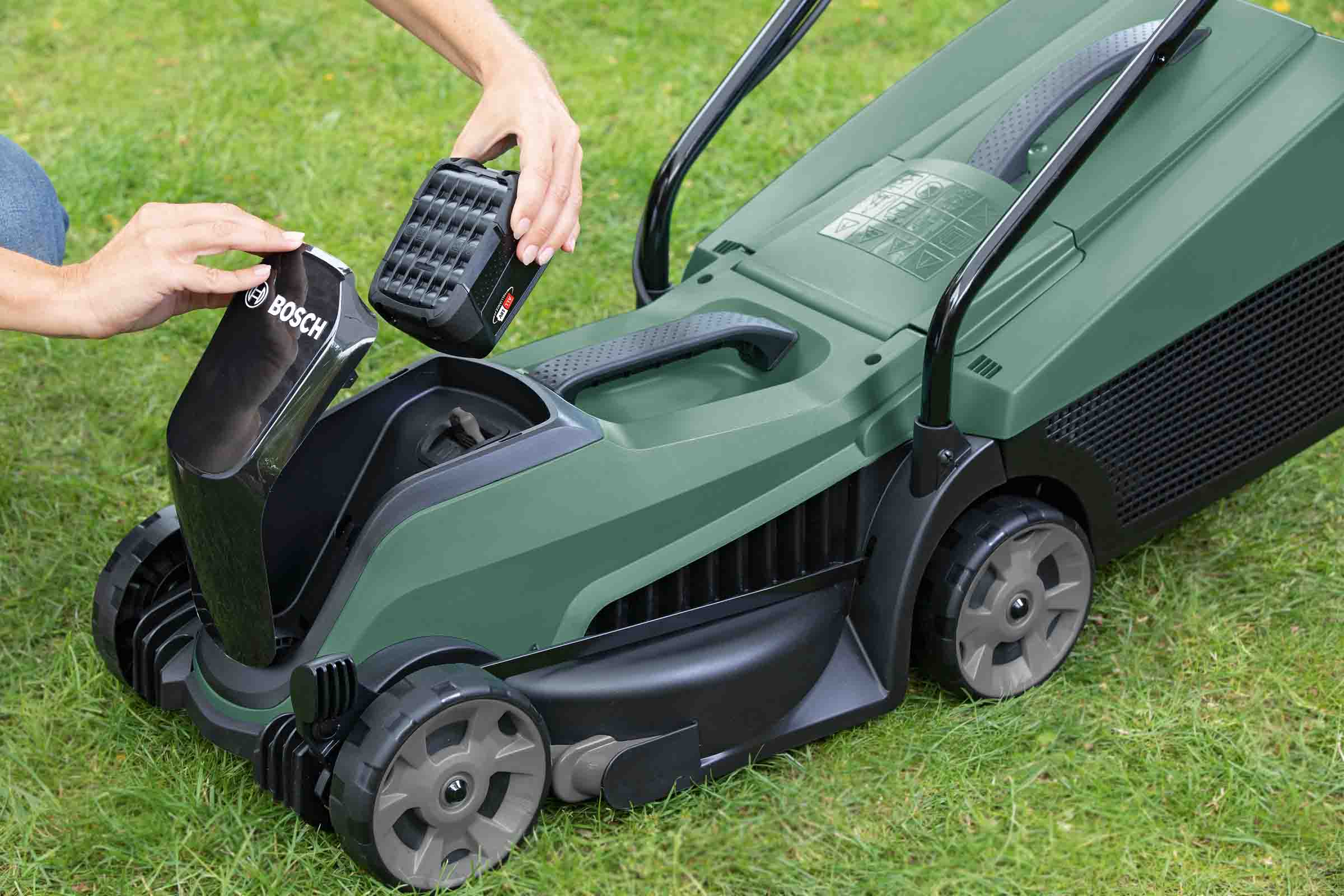 Vedere de sus a unei persoane care introduce un acumulator Bosch într-o mașină de tuns iarba.
