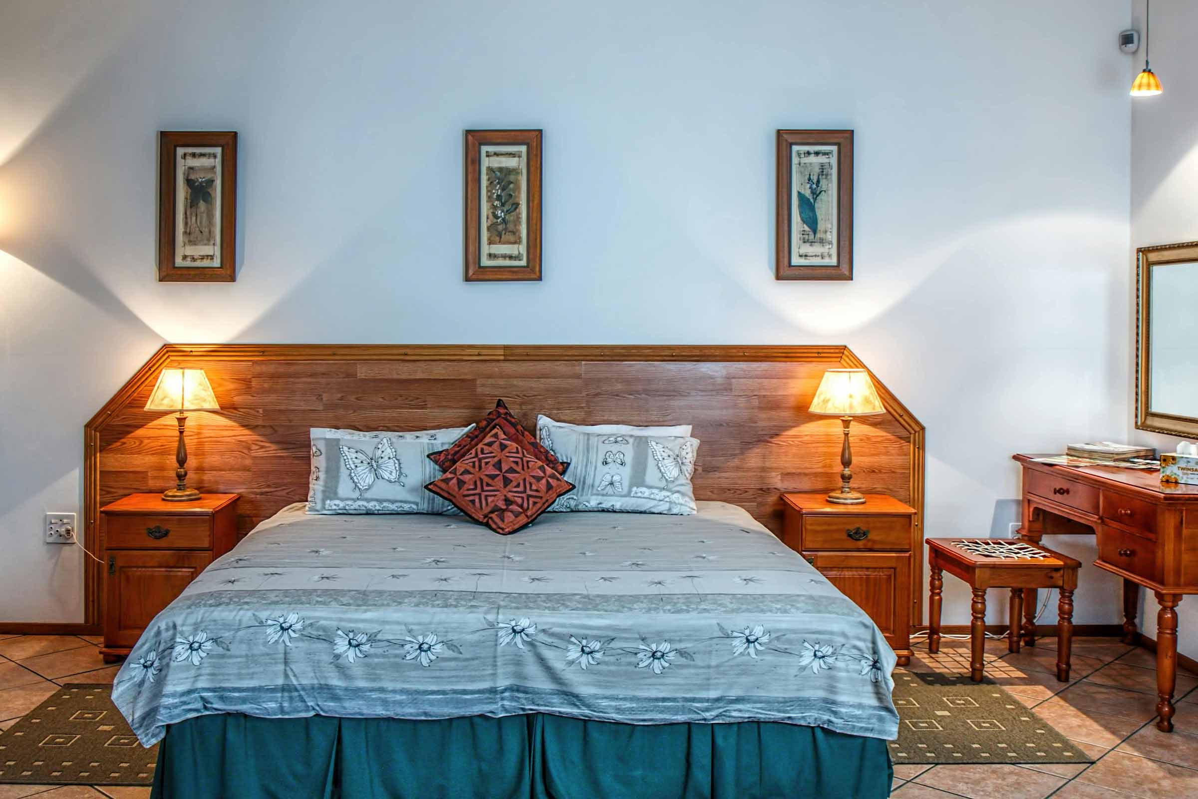 Dormitor cu pat din lemn, noptiere, lămpi și tablouri decorative pe perete
