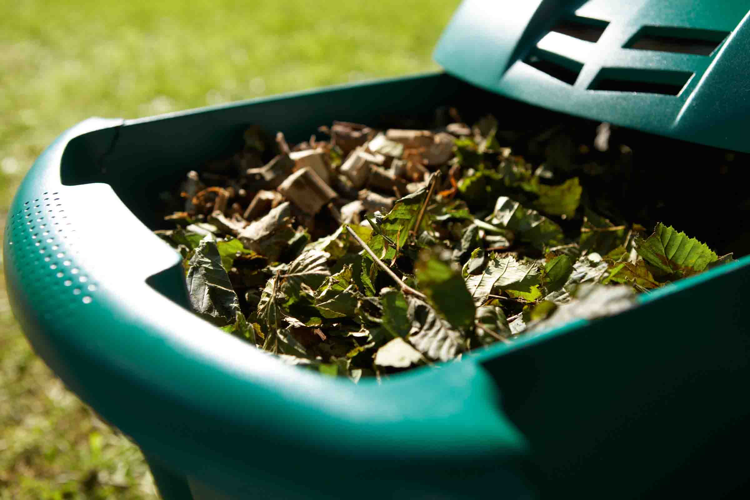 Recipient de compost deschis, plin cu deșeuri de grădină, precum frunze și bucăți de lemn.