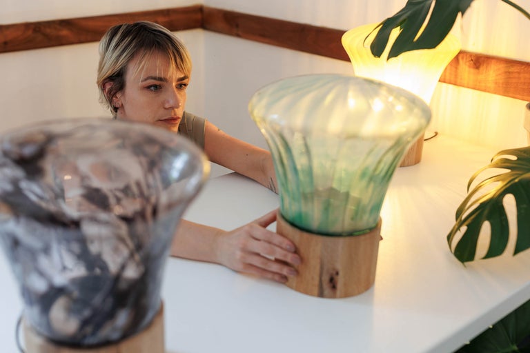 Scenă cu o femeie și două lămpi de masă cu bază de lemn și abajur de sticlă pe o masă.