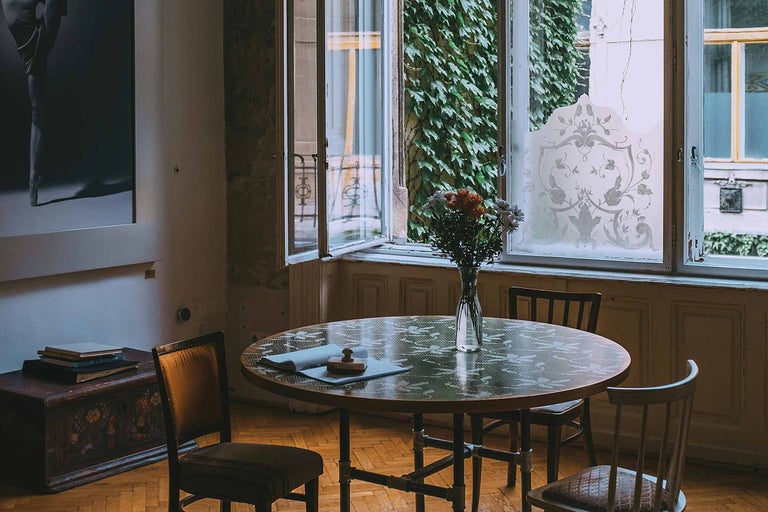 Amenajarea unei camere luminoase cu o masă rotundă, scaune și o fereastră cu decor floral