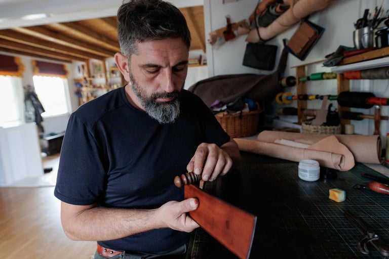 Un meșter prelucrează o bucată de piele cu o unealtă în atelierul său.