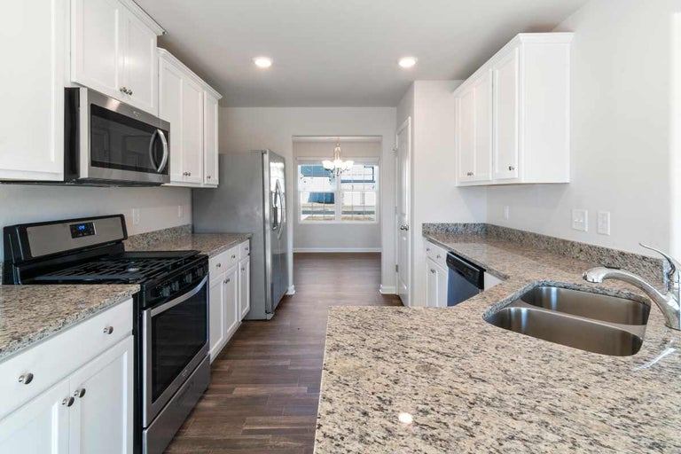 Bucătărie modernă și luminoasă, cu dulapuri albe, blaturi din granit și aparate din oțel inoxidabil, inclusiv aragaz.