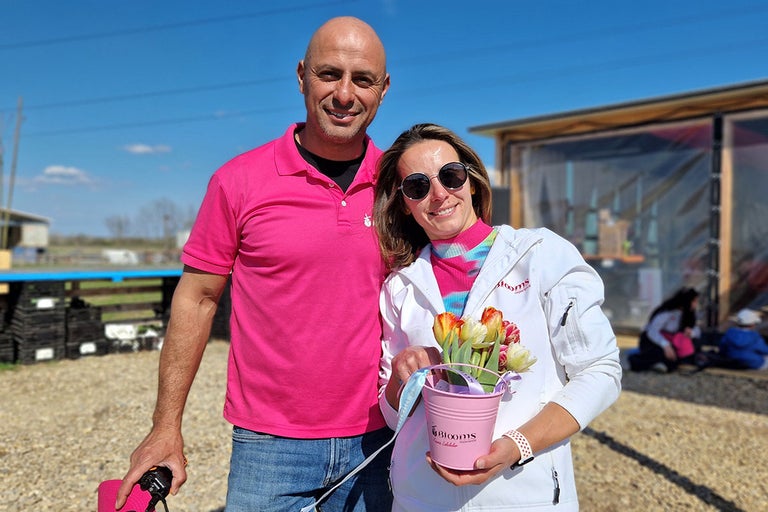 Cuplu zâmbitor ținând o găleată cu lalele afară.