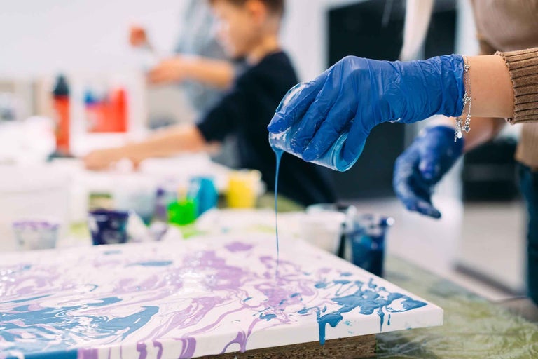 O persoană toarnă vopsea pe o pânză pentru un proiect artistic.