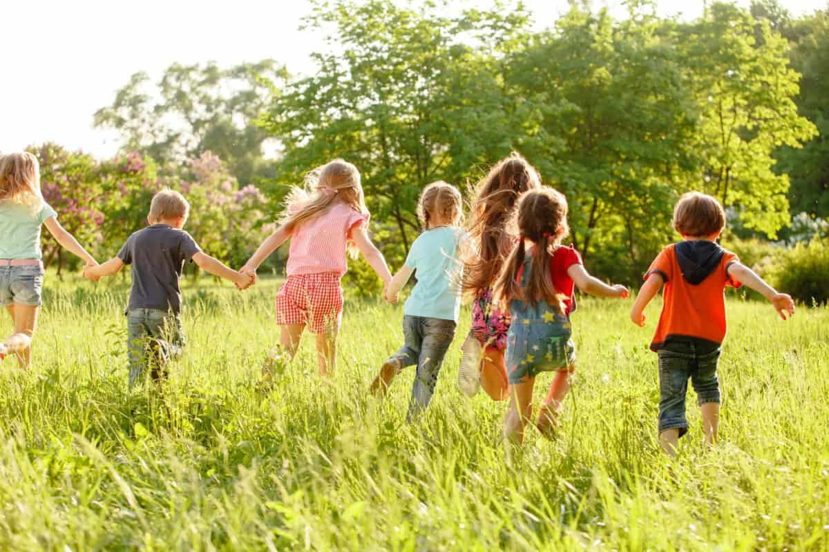 Un grup de copii aleargă ținându-se de mână pe un câmp verde.