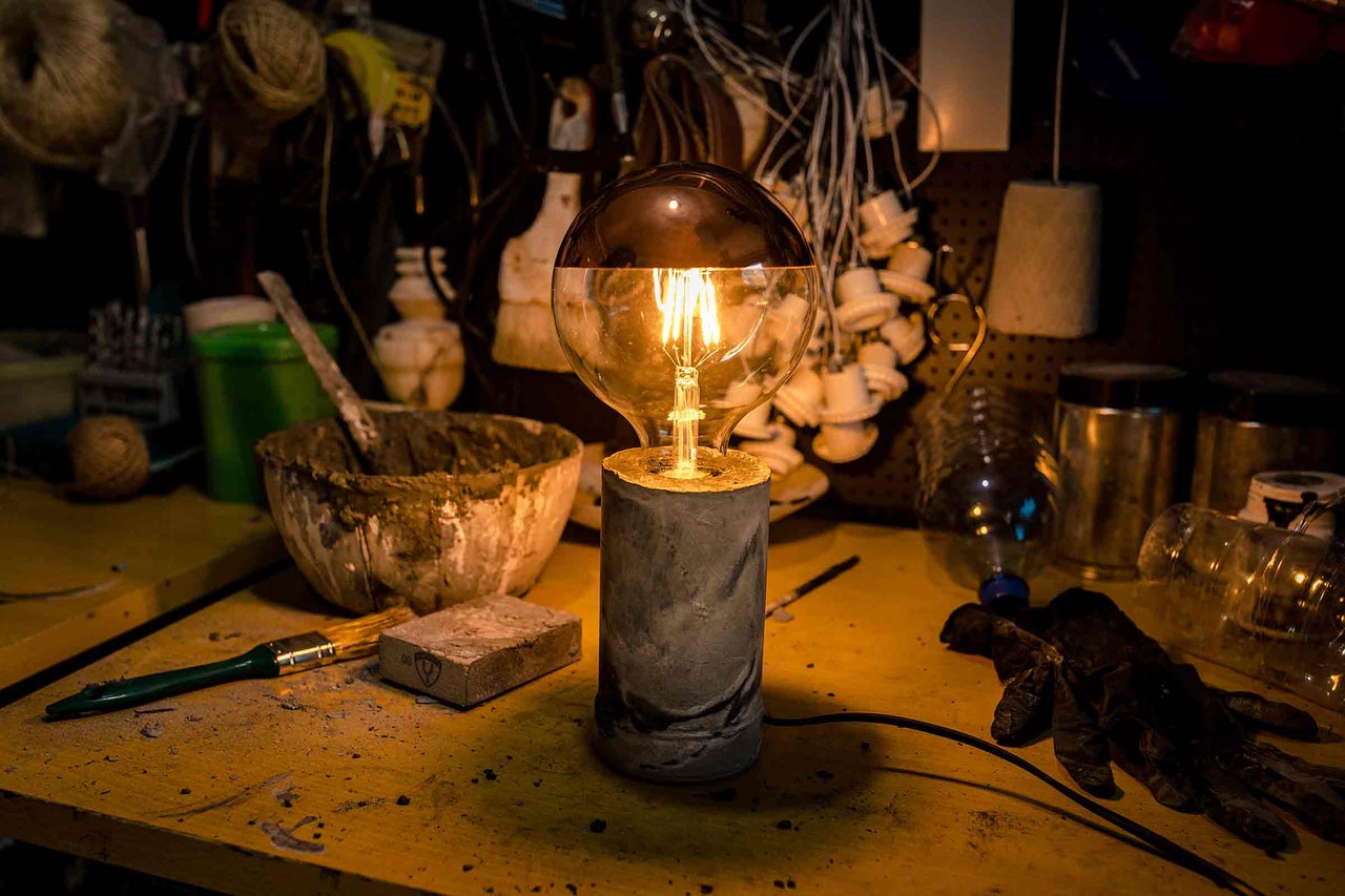 Lampă de masă decorativă cu bază din ciment și abajur din sticlă pe un banc de lucru.
