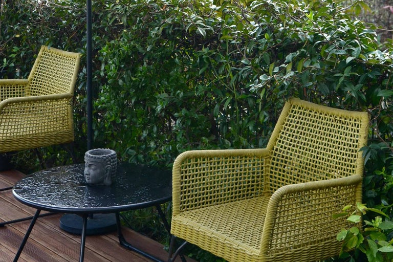 Scenă cu două scaune de răchită, o masă rotundă și un cap de Buddha pe o terasă.