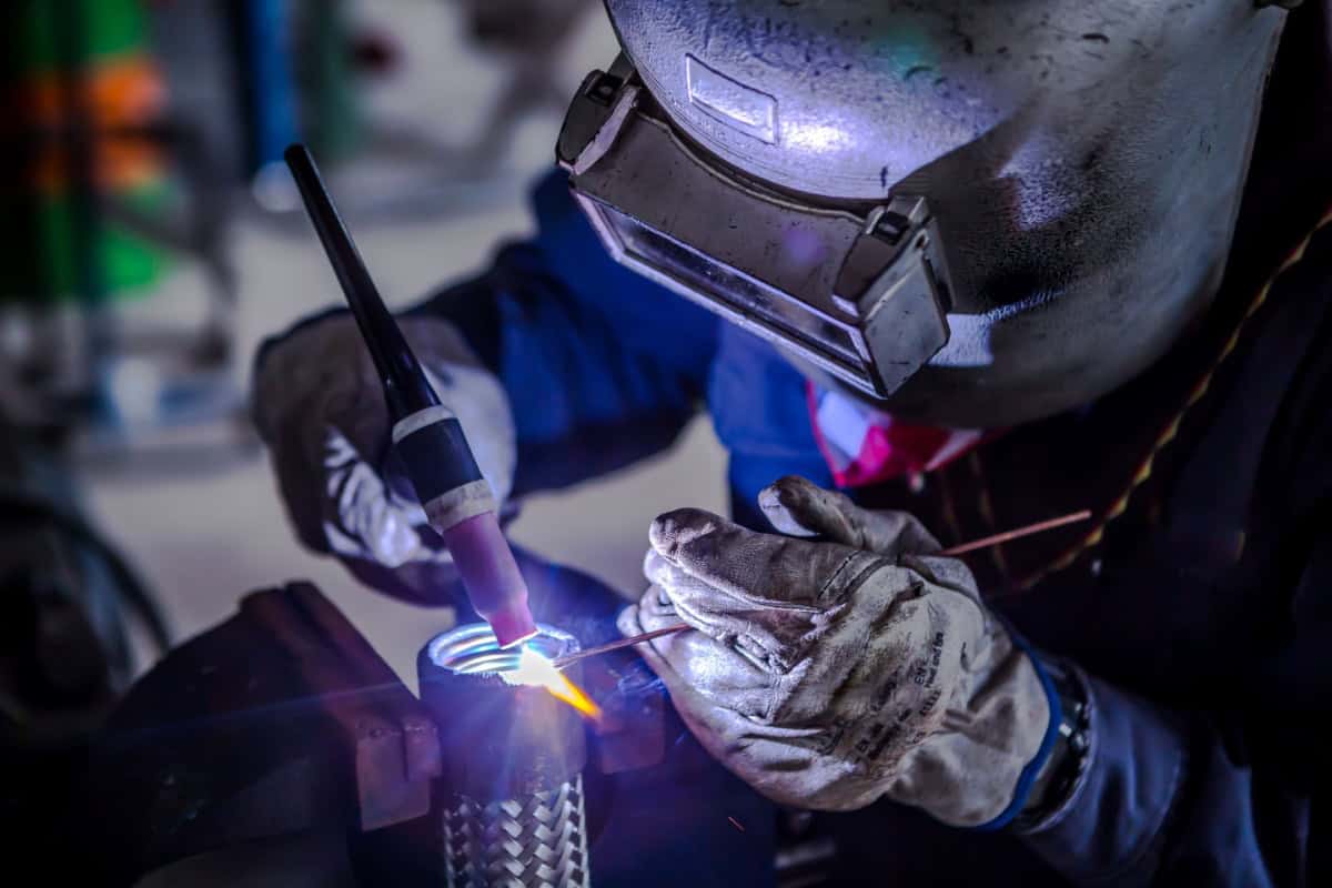 Un sudor cu cască de protecție și mănuși efectuează lucrări de sudură pe o piesă metalică.