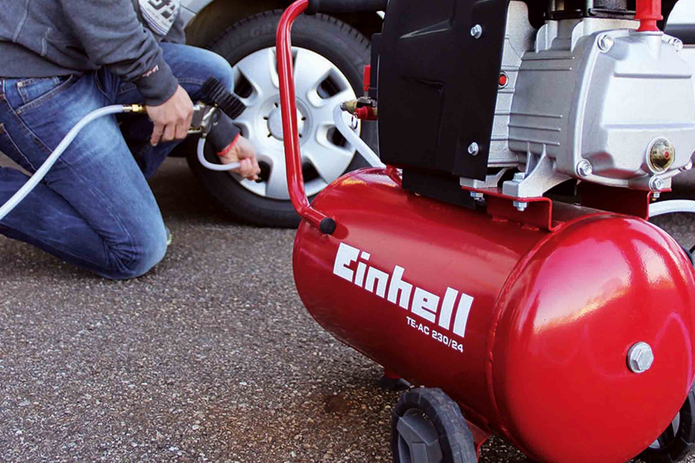 Un bărbat umflă o anvelopă de mașină cu un compresor roșu Einhell TE-AC 230/24.