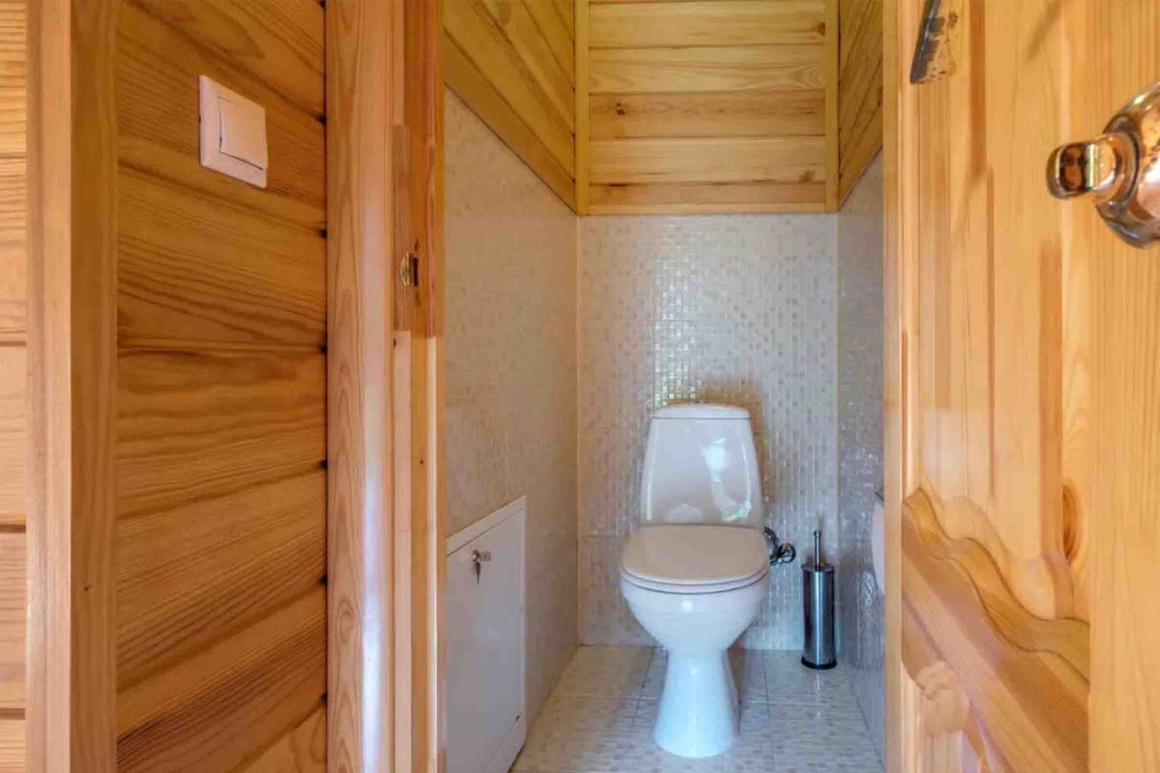 Toaletă mică cu vas WC pe pardoseală, mozaic și lambriuri din lemn natural.