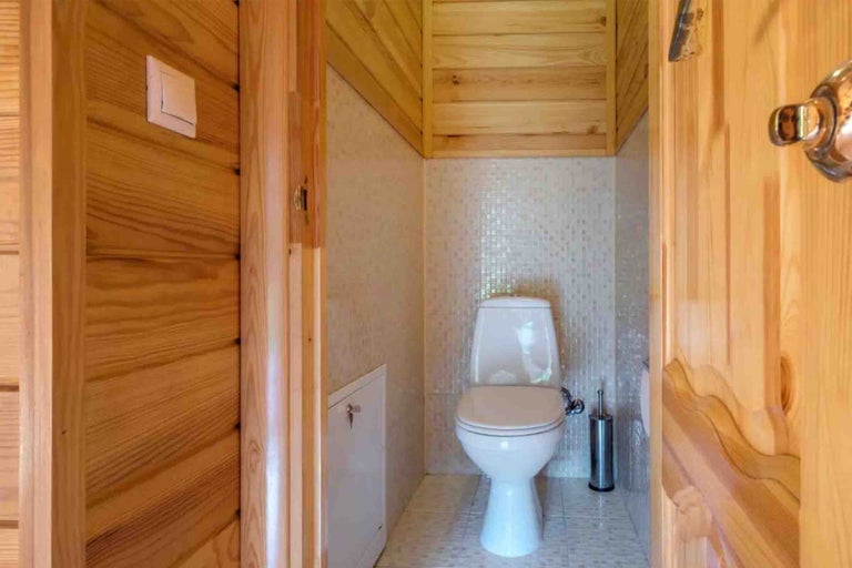 Toaletă mică cu vas WC pe pardoseală, mozaic și lambriuri din lemn natural.