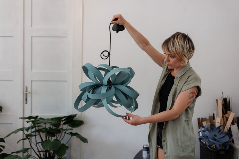 Femeie ține o lampă suspendată în formă de floare într-o cameră.