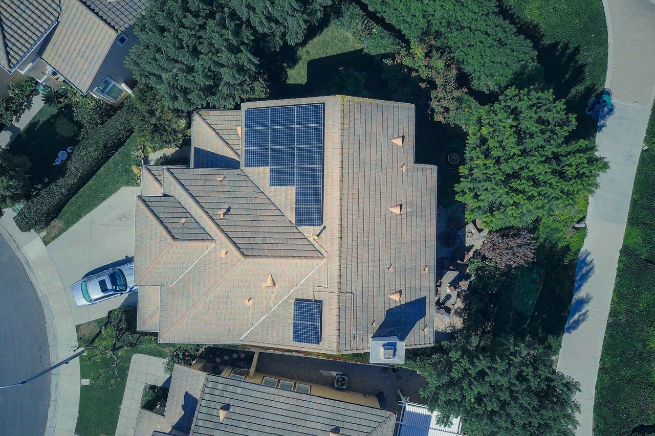 Vedere aeriană a unei case cu acoperiș din țiglă și panouri solare într-o zonă rezidențială.